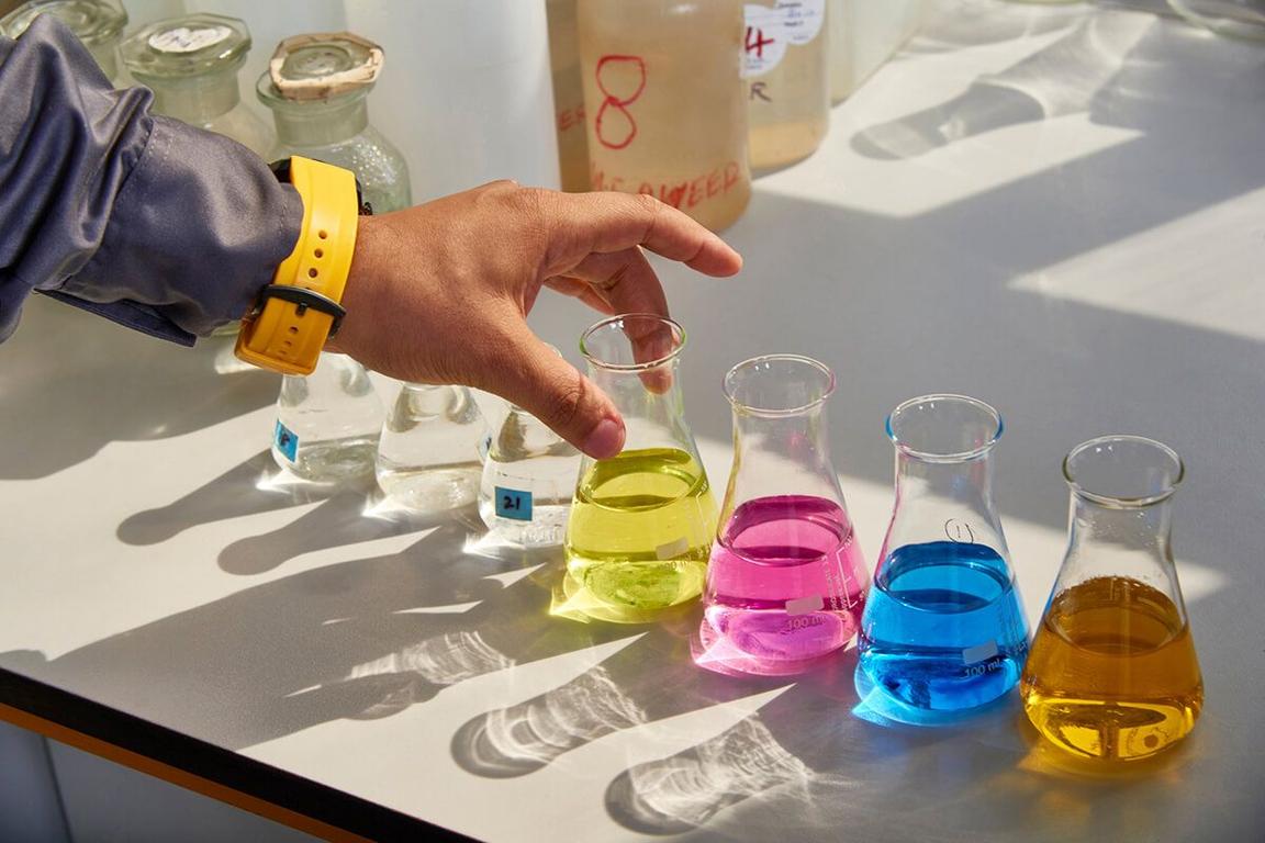 worker's hand in lab setting with fluid-filled beakers in various colors