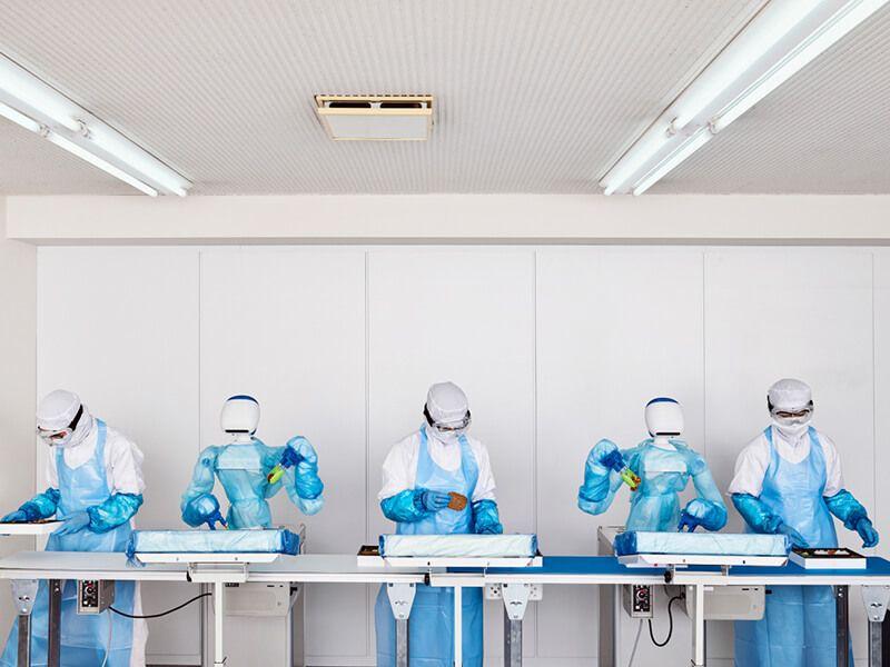 humans in clean room garments preparing food alongside robots in factory