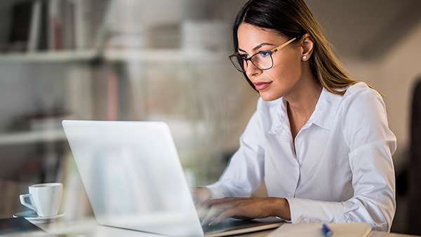 Woman using a notebook computer with a cup on her side