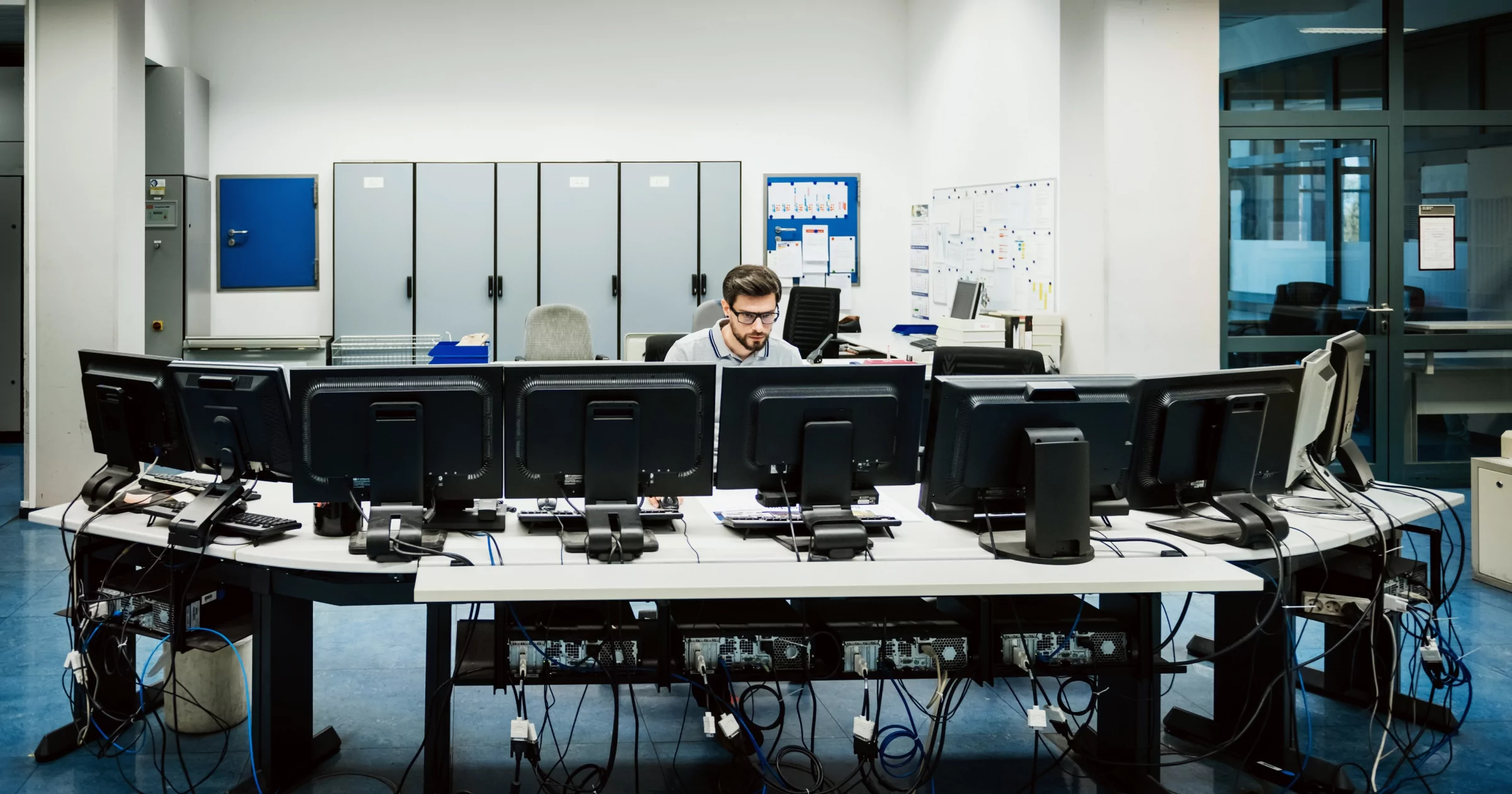 Engineer is working behind several work stations in a big control room