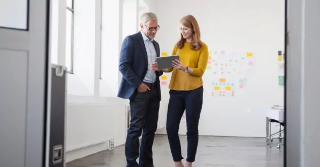 Two coworkers standing in middle of office looking at ipad together