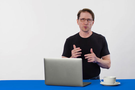 Hombre hablando junto a una computadora portátil abierta.