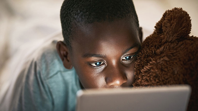 Young boy using a digital tablet at night in bed