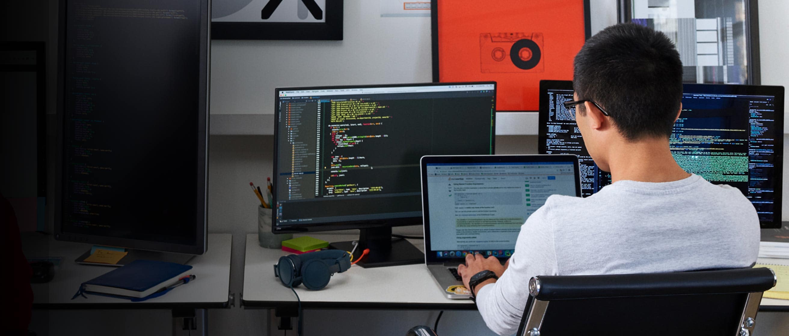 seorang pemprogram yang sedang bekerja dengan tiga monitor