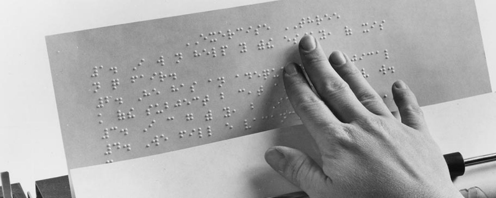 A hand on an embossed sheet of paper in a braille typewriter, 1974