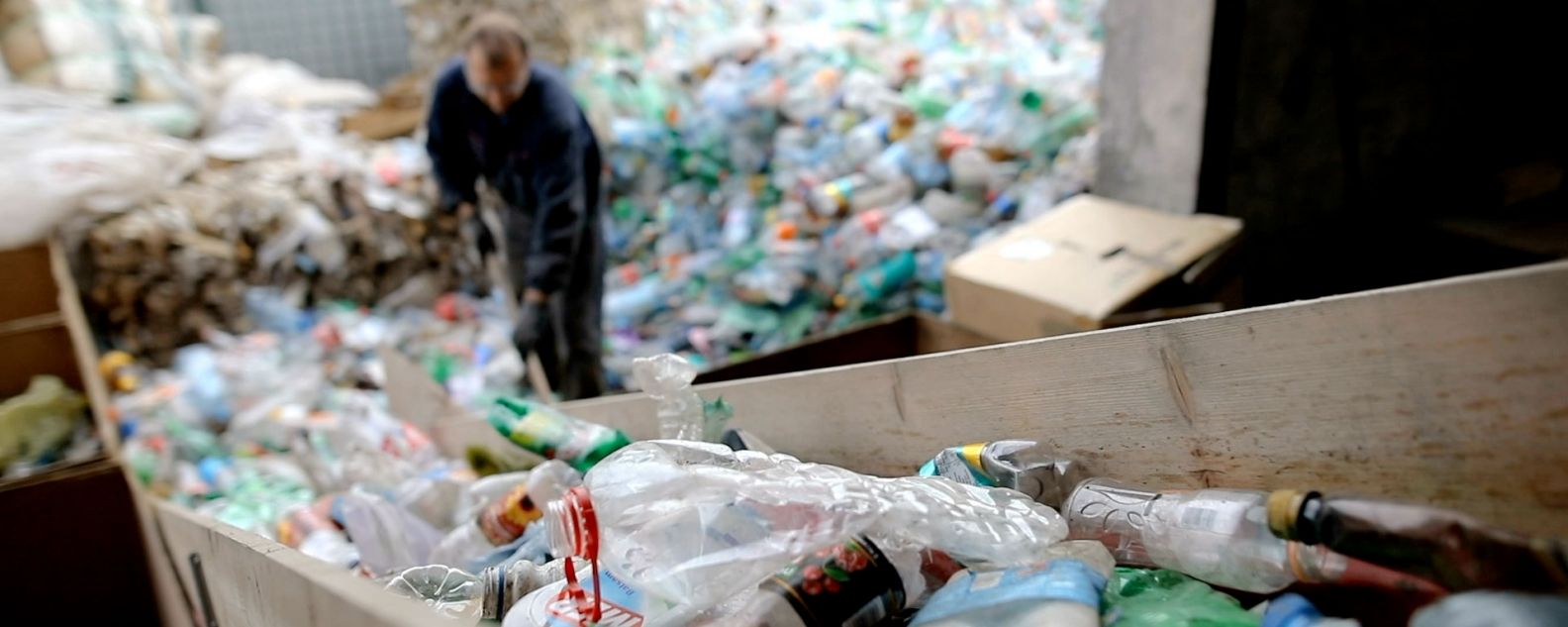 In einer Recyclingfabrik schaufelt ein Arbeiter mit einer Schaufel Plastikflaschen zum Recycling