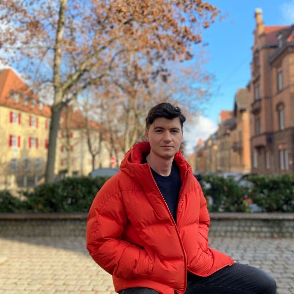 IBM employee sitting on a rock wearing a red jacket with yellow buildings in the background