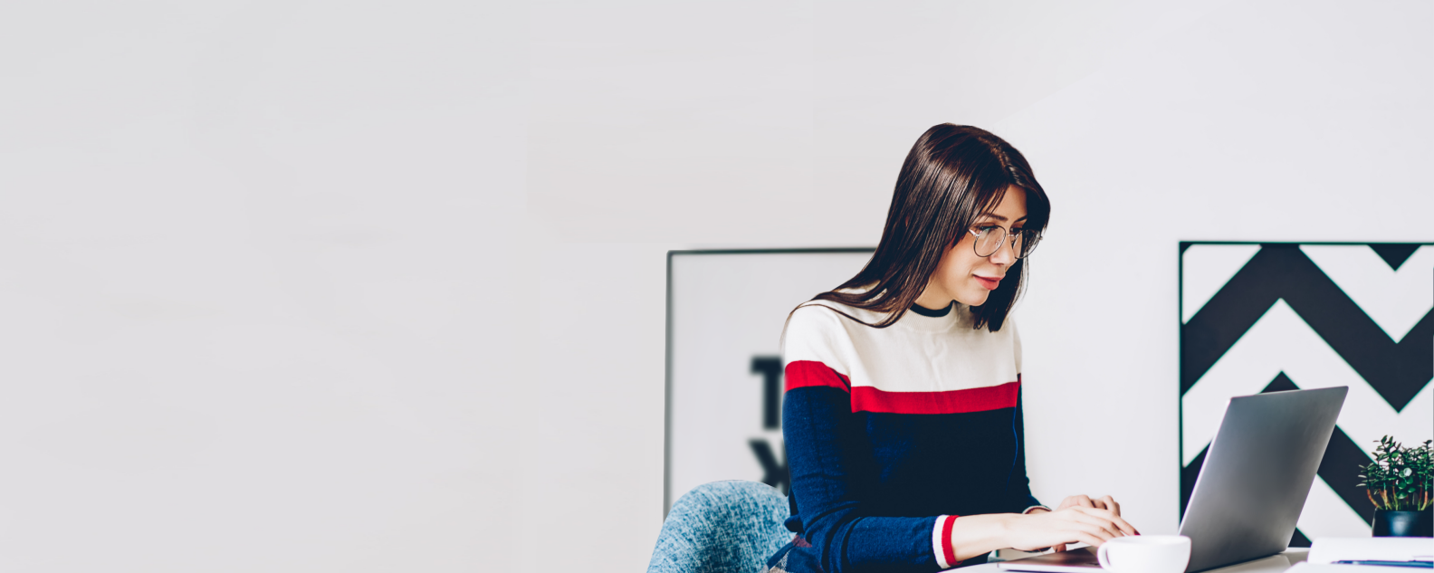 Uma jovem estudante usando óculos digitando informações para um trabalho de faculdade no teclado de um notebook moderno e usando Internet wireless em um apartamento elegante