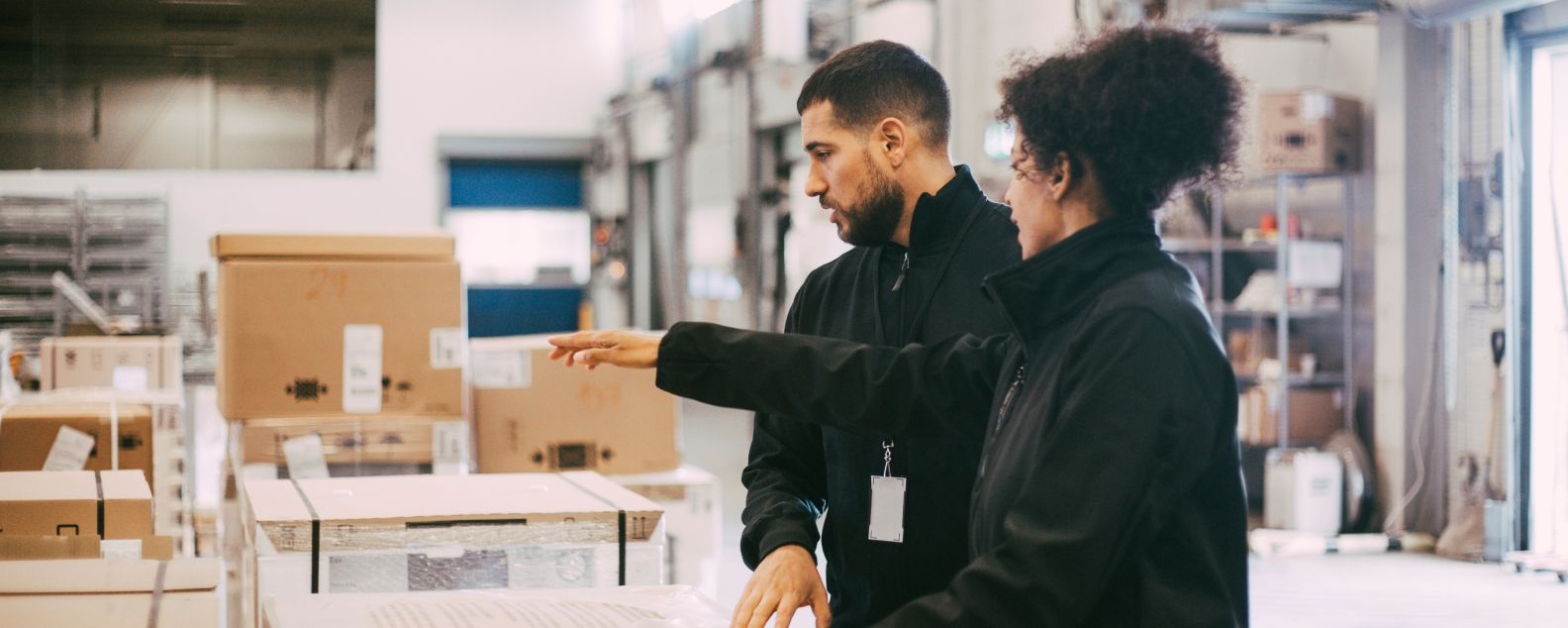 Two warehouse workers using a tablet and one is pointing at boxes