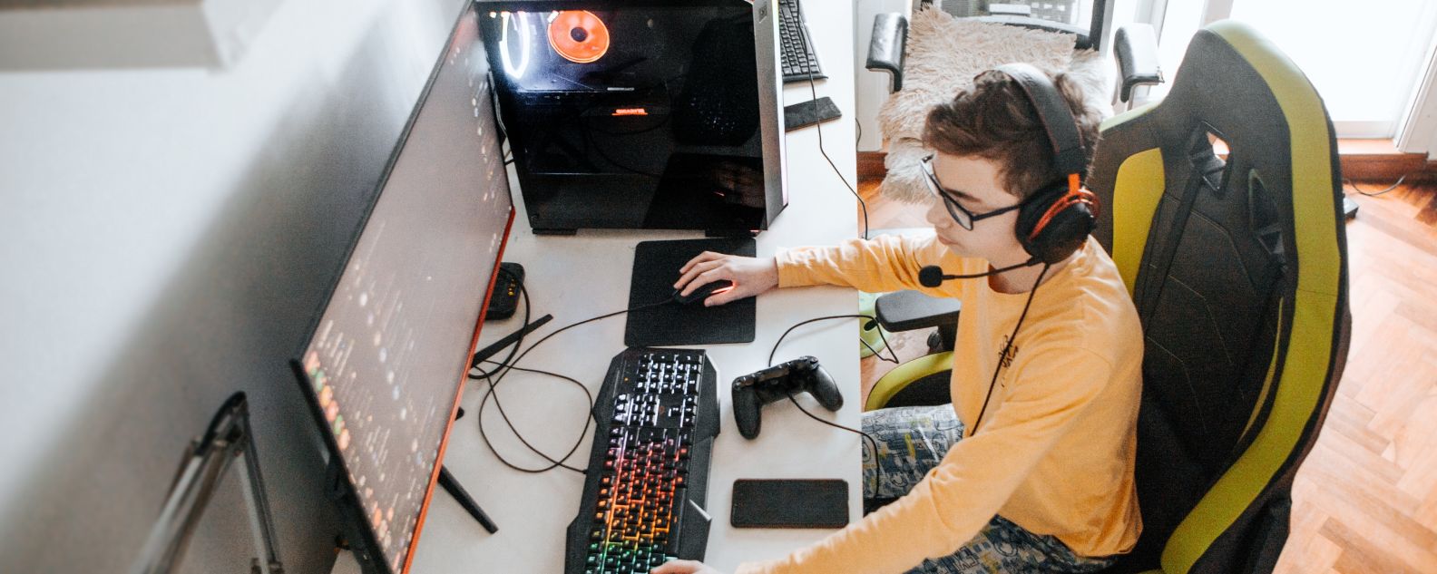 Image of teenaged boy, with headphones on his head, playing video games at home