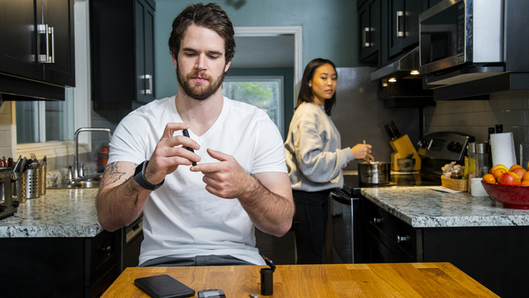 Person sitting at table in kitchen uses medical device on finger