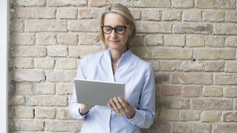 Person using tablet while leaning against brick wall