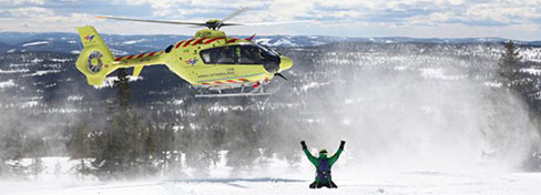 Inflight helicopter ambulance with person standing below in snow
