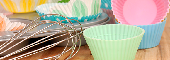 Colorful paper cupcake liners with whisk and baking sheet, sitting on table