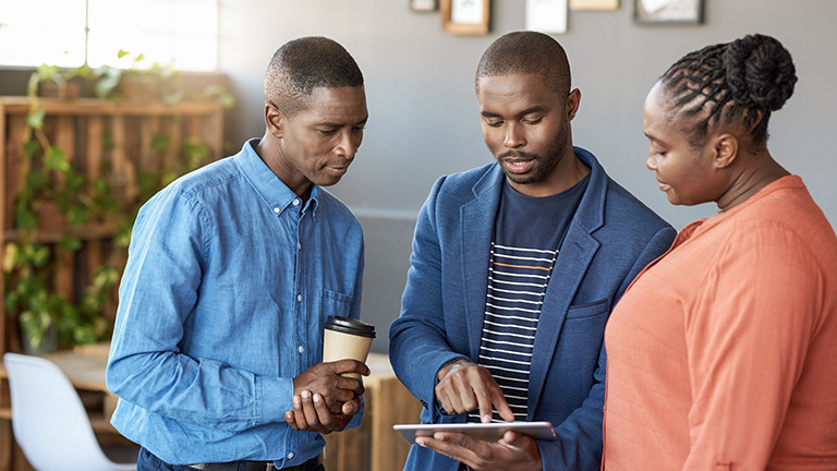 Three people looking down at a tablet