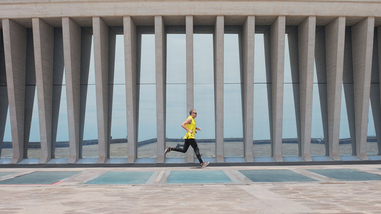 A person running on a track alongside a modernist concrete building