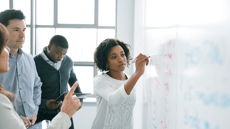 Woman writing on white board with coworkers collaborating with her