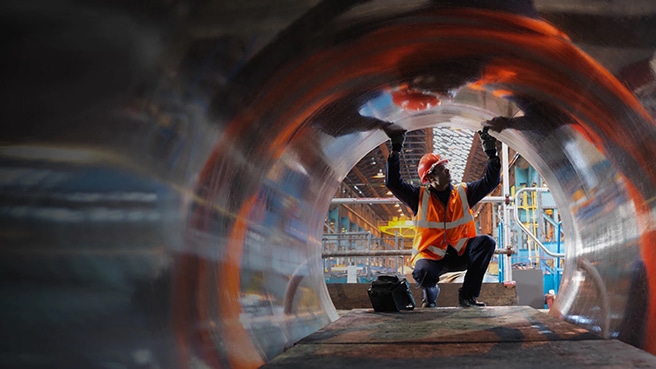 An engineer in a hard hat inspecting large diameter steel pipe