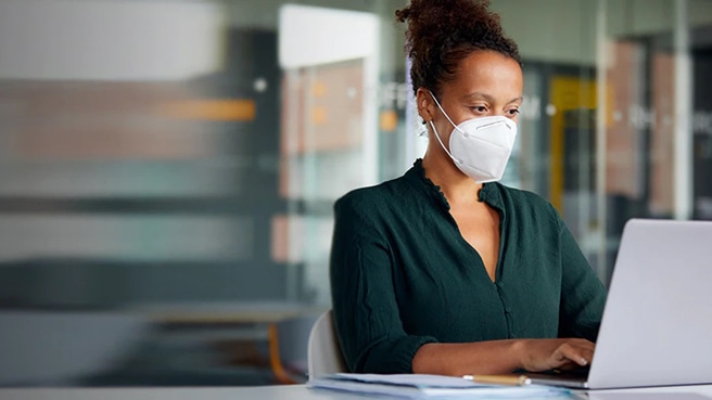 A worker wearing a protective face mask sitting at a desk