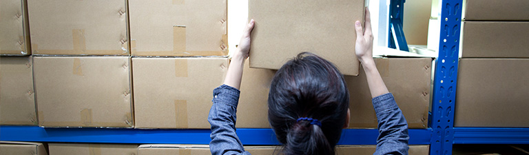 A woman pulls a box from a large shelf of packages